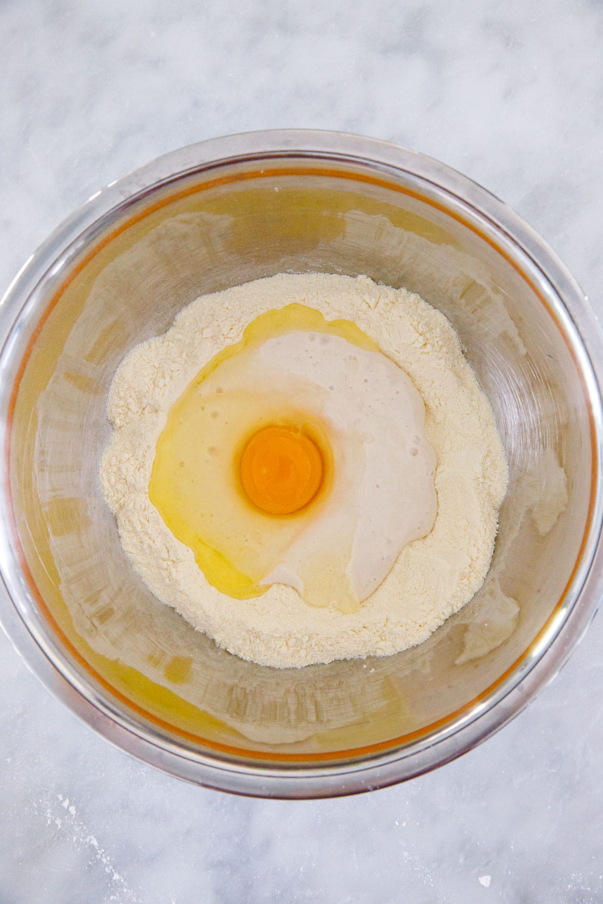 Overhead view of metal bowl with semolina flour, sourdough starter, and an egg before mixing.