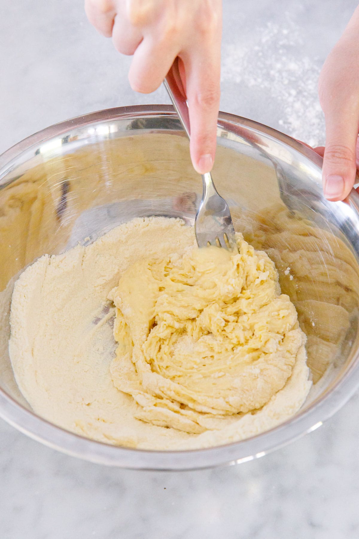 Mixing sourdough pasta dough in a metal bowl with a fork.
