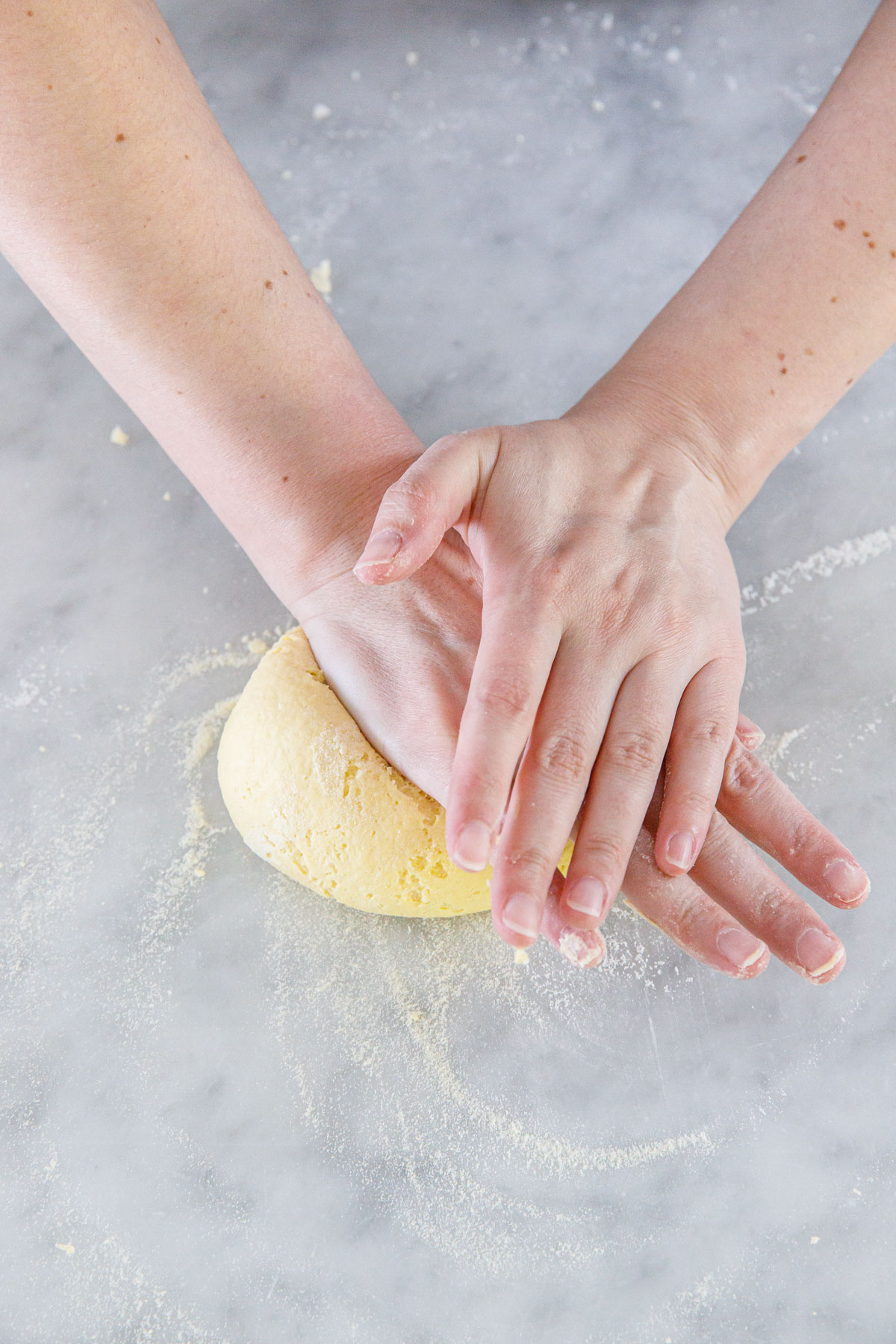 Kneading homemade pasta dough on a marble surface until it is smooth.