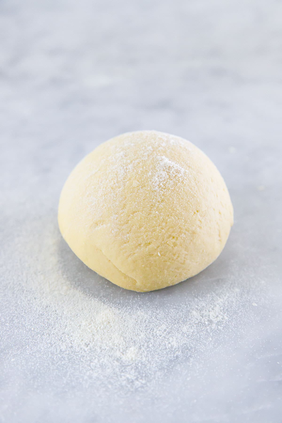 Freshly kneaded ball of homemade sourdough pasta dough, dusted with semolina on a marble surface.