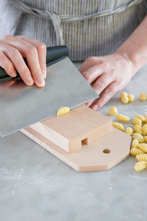 Shaping gnochetti sardi pasta, using a bench scraper and a gnocchi board.