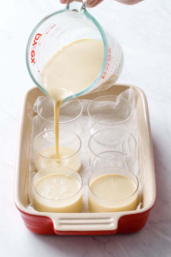 Pouring custard into glass ramekins in a red baking dish