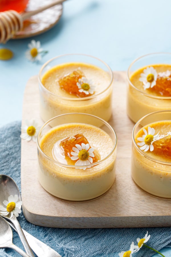 Honey pots de creme served in glass ramekins, topped with a triangle of honeycomb and fresh chamomile flowers
