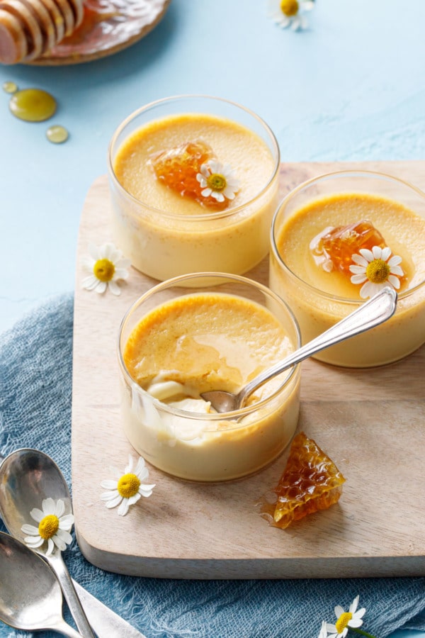 Three glass ramekins with Honey Vanilla Pots de Crème, a spoonful in the front one to show texture.