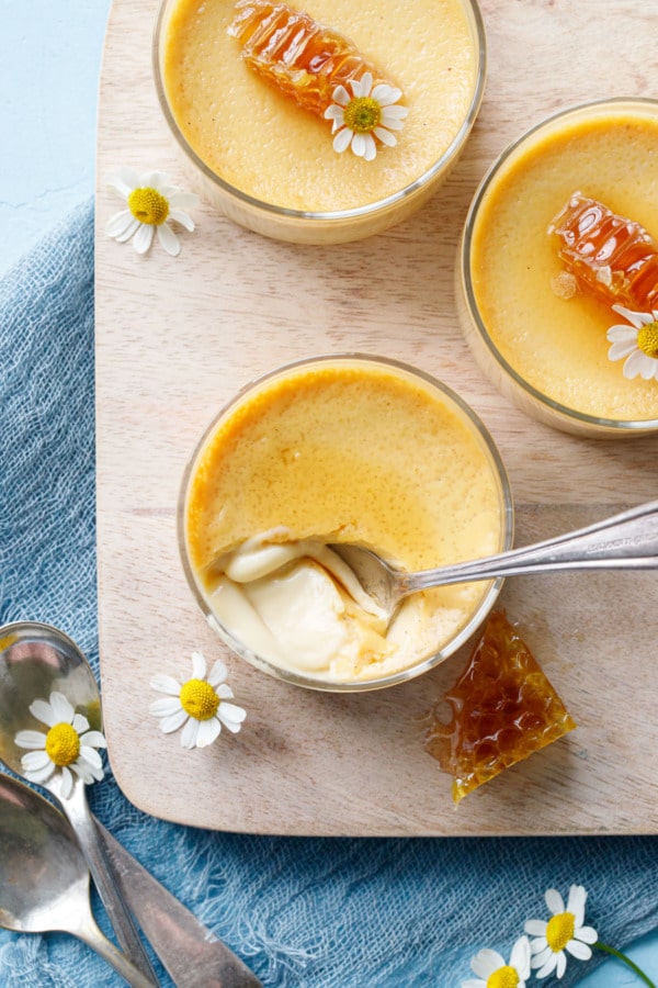 Overhead, glass ramekin with honey pot de creme custard, and a spoon scoop to show the extra smooth texture