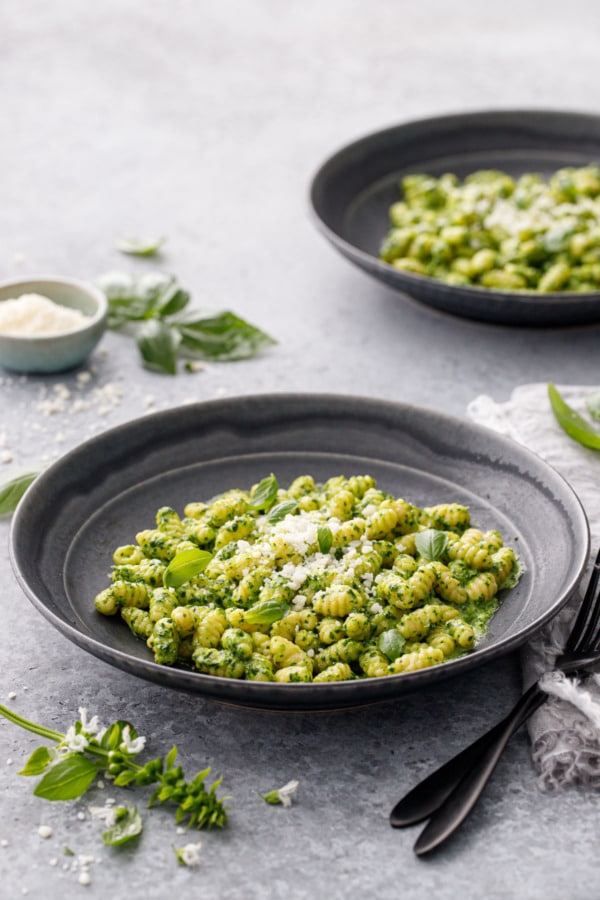 Two black bowls with homemade gnochetti with pesto sauce, black utensils and basil leaves