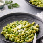 Gnochetti with bright green pesto sauce in black ceramic bowls and black forks on a gray background