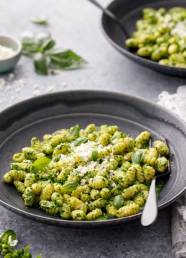 Gnochetti with bright green pesto sauce in black ceramic bowls and black forks on a gray background