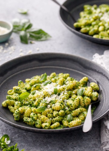 Gnochetti with bright green pesto sauce in black ceramic bowls and black forks on a gray background