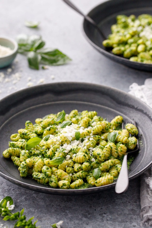 Gnochetti with bright green pesto sauce in black ceramic bowls and black forks on a gray background