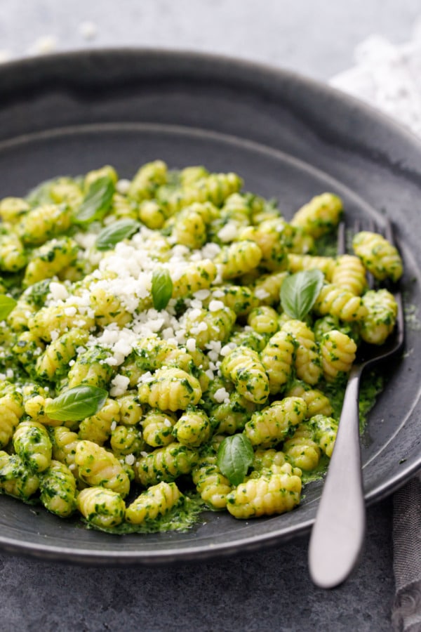 Closeup, homemade gnochetti sardi pasta with bright green pesto sauce and grated pecorino, in a black bowl with matte black fork