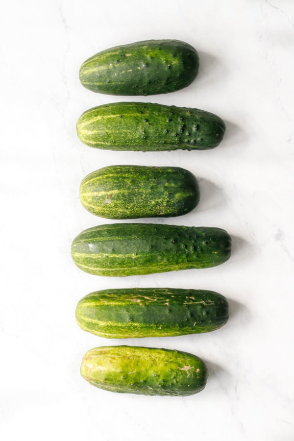 Overhead gradient of cucumbers arranged in a row on a white marble background