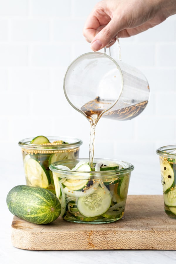 Pouring the pickle brine into glass jars packed with sliced cucumbers