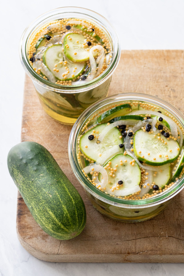 Two jars of freshly made Bread & Butter Refrigerator Pickles on an old wood board with a whole cucumber on the side