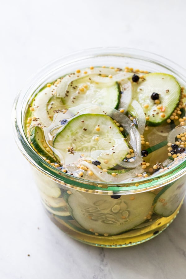 Closeup, open jar with freshly made Bread & Butter Refrigerator Pickles, filled with brine and whole mustard seeds and peppercorns.