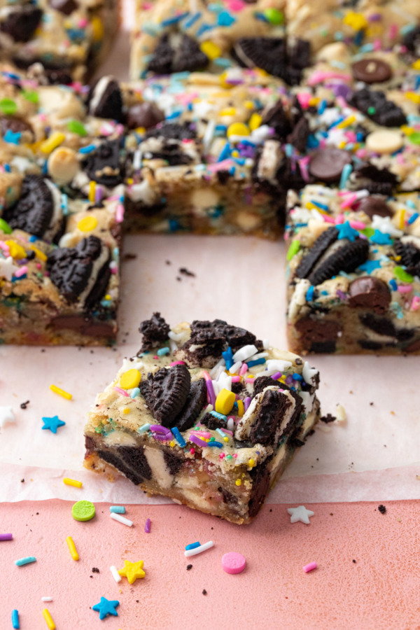 Square of party blondies cut to show a perfect cross section of what's inside, on a pink background