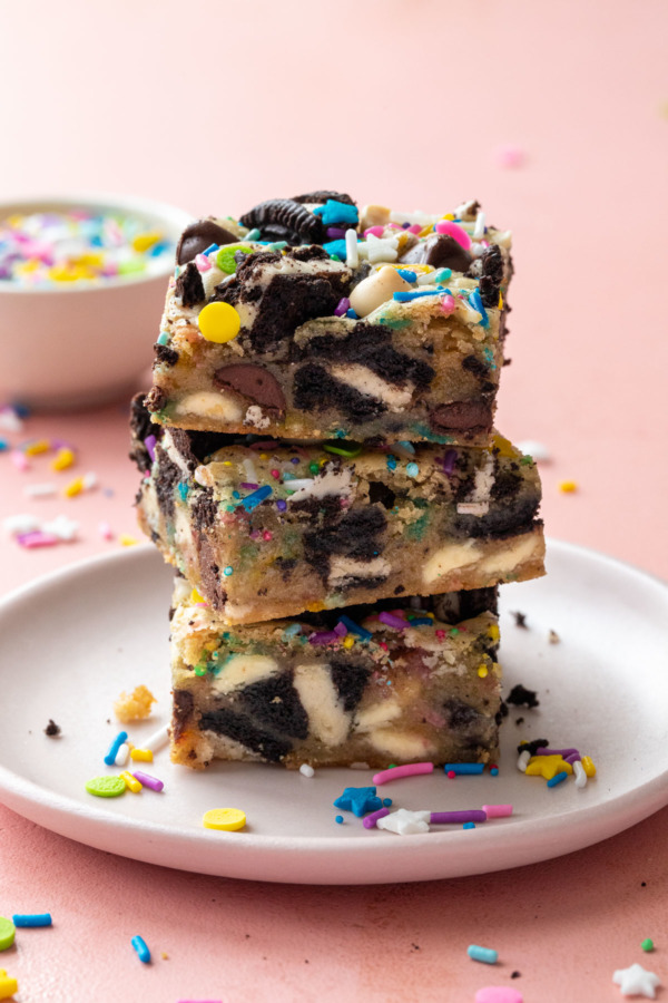 Closeup sideview, stack of three sprinkle party blondies showing a cross-section of the mix-ins