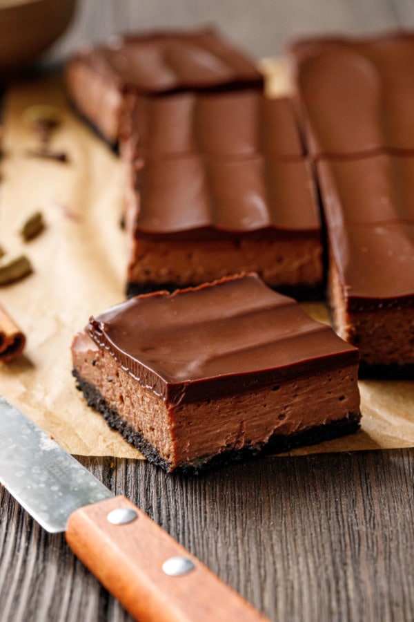 Closeup cut square of Chocolate Chai Cheesecake Bar, on parchment with a knife in the foreground