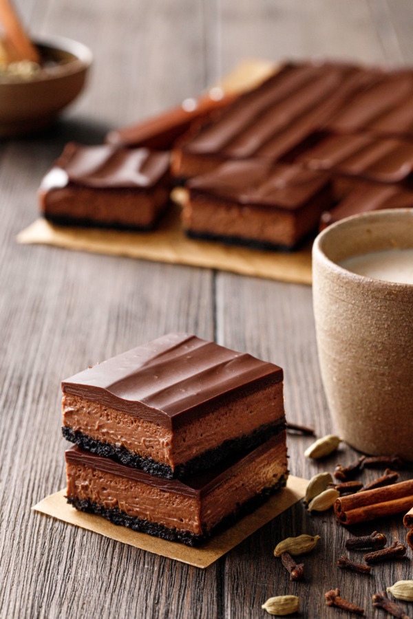 Stack of two Chocolate Chai Cheesecake Bars, with cup of chai and cut bars in the background