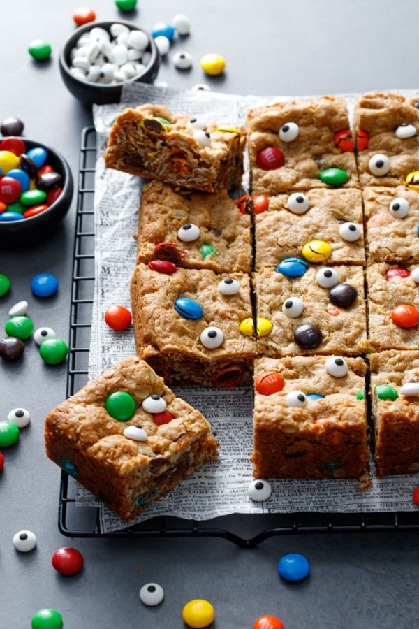 Monster Cookie Bars, topped with M&Ms and candy eyeballs cut into squares on a dark background