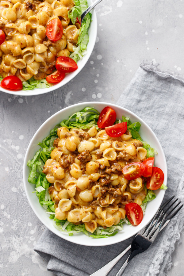 Overhead, two bowls of Taco Shells & Cheese served on beds of iceberg lettuce with quartered cherry tomatoes