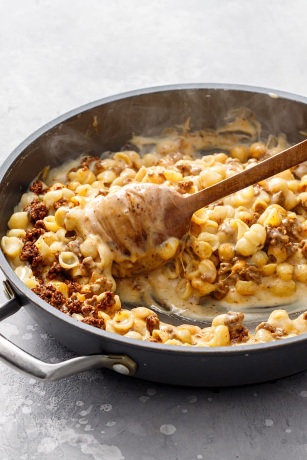 Large skillet with Taco Shells & Cheese, stirring with a wooden spoon to show the ultra creamy texture