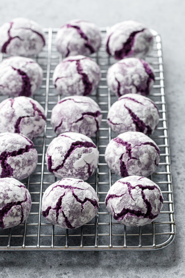 Silver wire baking rack with even rows of ube amaretti crinkle cookies coated in powdered sugar