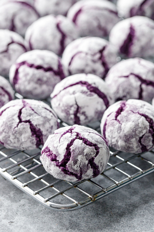 Closeup of ube amaretti cookie on a wire rack, showing the purple crinkle texture and powdered sugar coating.