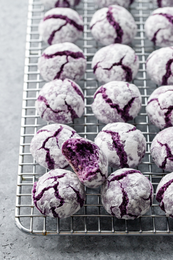 Wire rack with rows of ube amaretti cookies, with a bite out of one to show the interior texture.