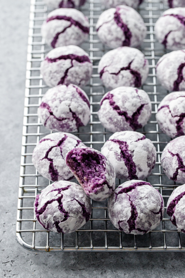 Wire rack with rows of ube amaretti cookies, with a bite out of one to show the interior texture.