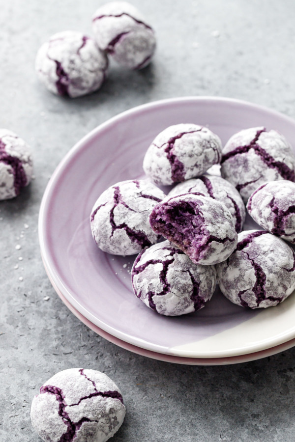 Purple plate with pile of purple sweet potato amaretti crinkle cookies on a gray background