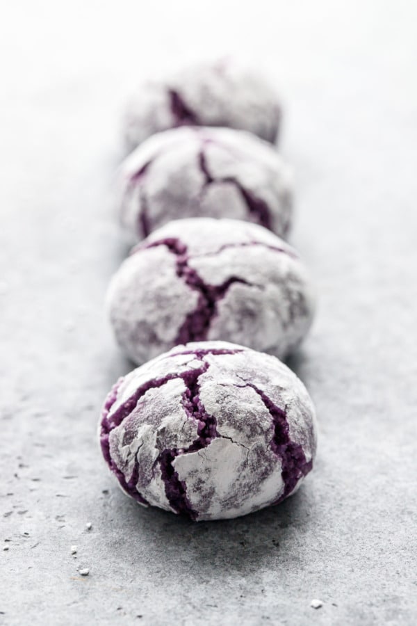 Closeup with narrow depth of focus, row of ube amaretti crinkle cookies on a gray background.