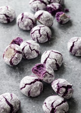 Messy scattered ube amaretti crinkle cookies on a gray background