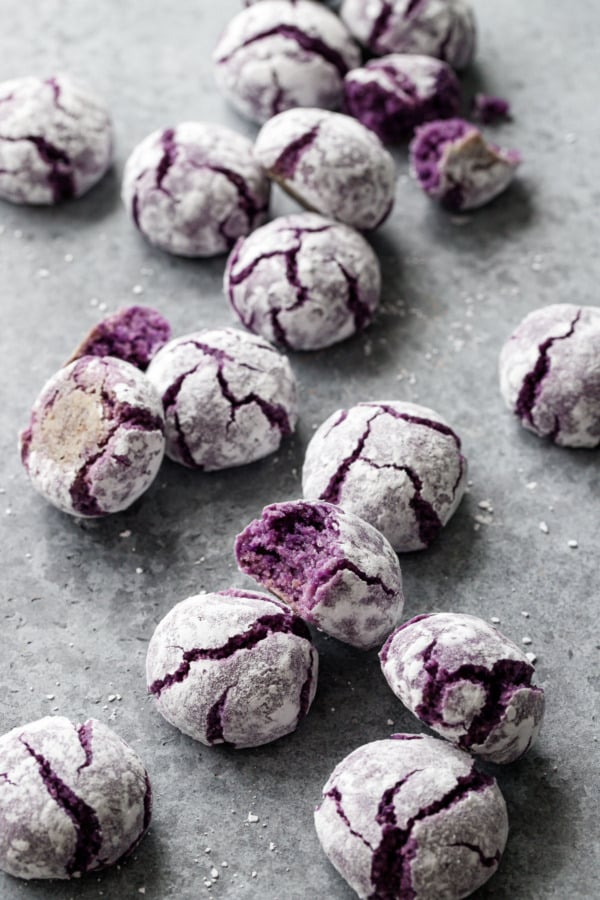 Messy scattered ube amaretti crinkle cookies on a gray background