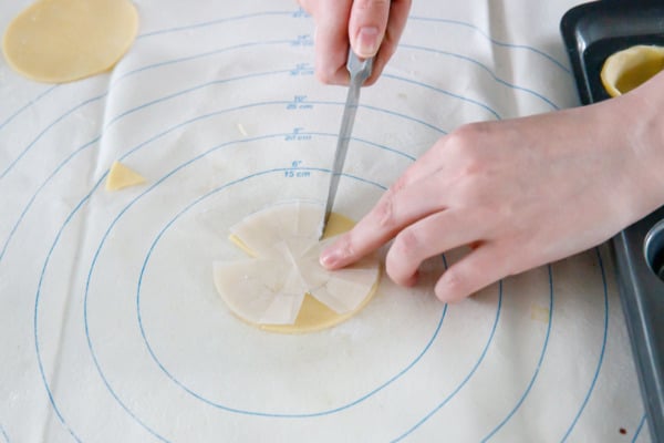 Cutting a small round of pie crust with a parchment template to fit in a mini muffin tin