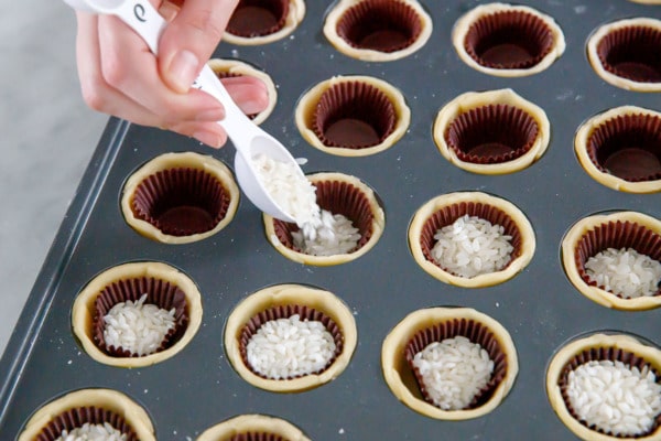 Mini muffin tin with pie crusts, with paper candy cups filled with rice to weight them down as they bake