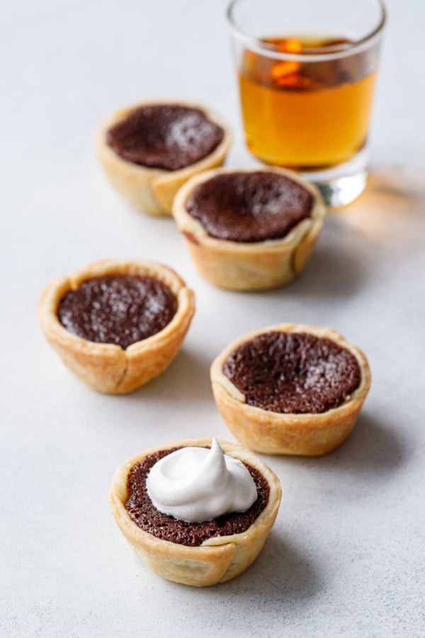 Five Mini Bourbon Fudge Pies on a gray background with a shot of bourbon