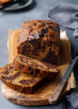 Sliced loaf of Pumpkin Chocolate Swirl Bread on an olivewood bread board on a dark gray background