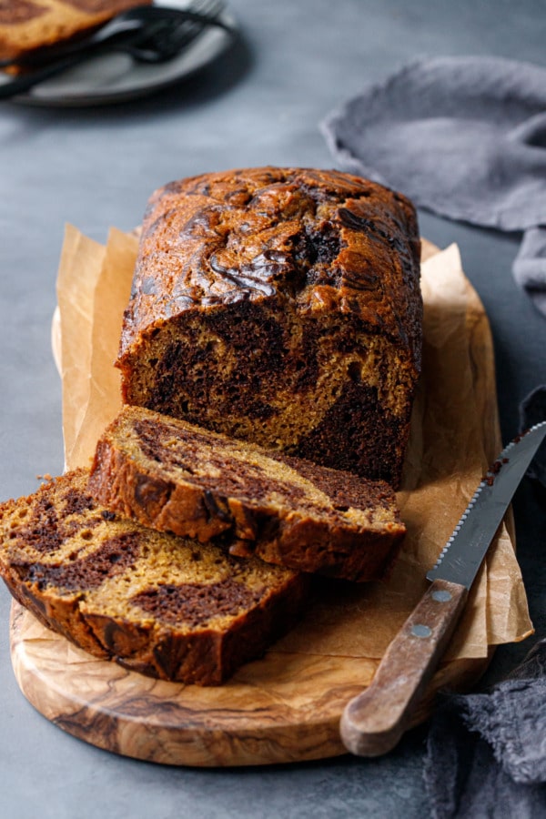 Sliced loaf of Pumpkin Chocolate Swirl Bread on an olivewood bread board on a dark gray background