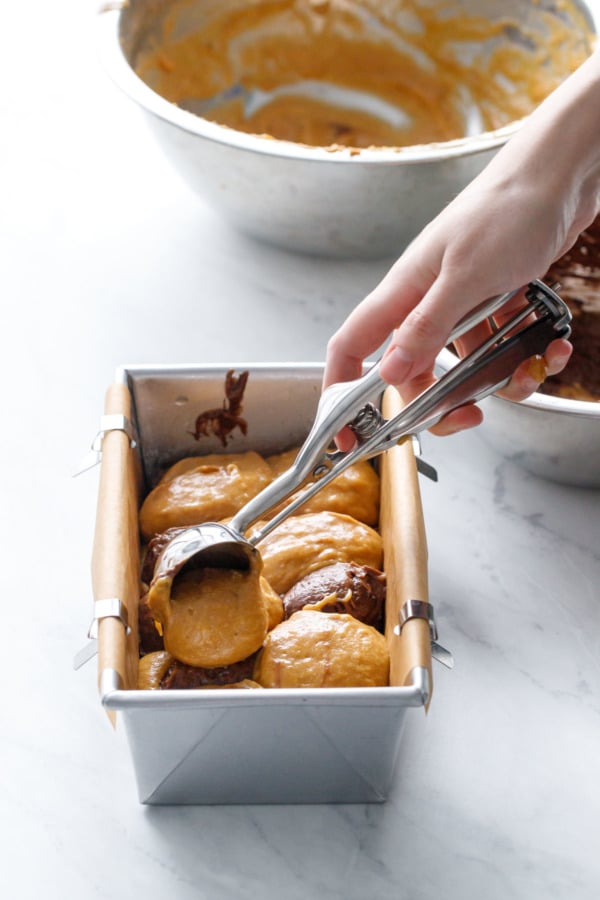 Alternating scoops of pumpkin and chocolate batter in a parchment lined bread tin to achieve the marbled effect