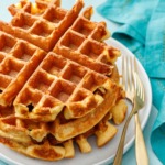 Stack of three thick Belgian Savory Cheddar Cheese Waffles on a white plate, turquoise background and gold forks