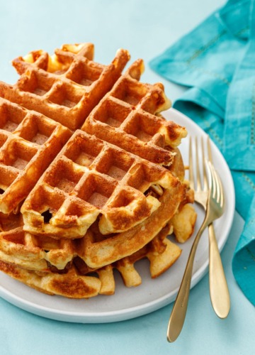 Stack of three thick Belgian Savory Cheddar Cheese Waffles on a white plate, turquoise background and gold forks