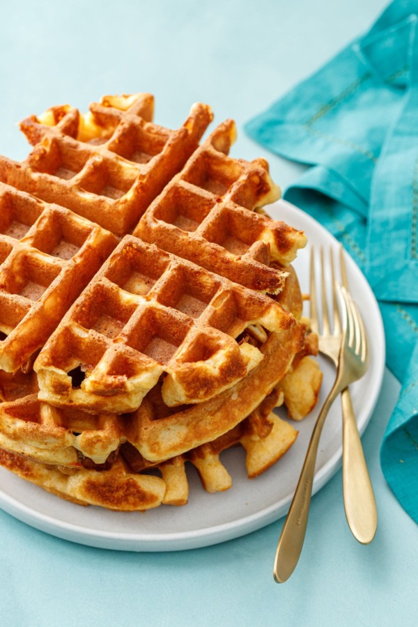 Stack of three thick Belgian Savory Cheddar Cheese Waffles on a white plate, turquoise background and gold forks