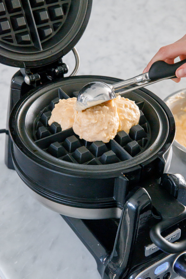 Using a cookie scoop to portion batter onto the waffle maker.