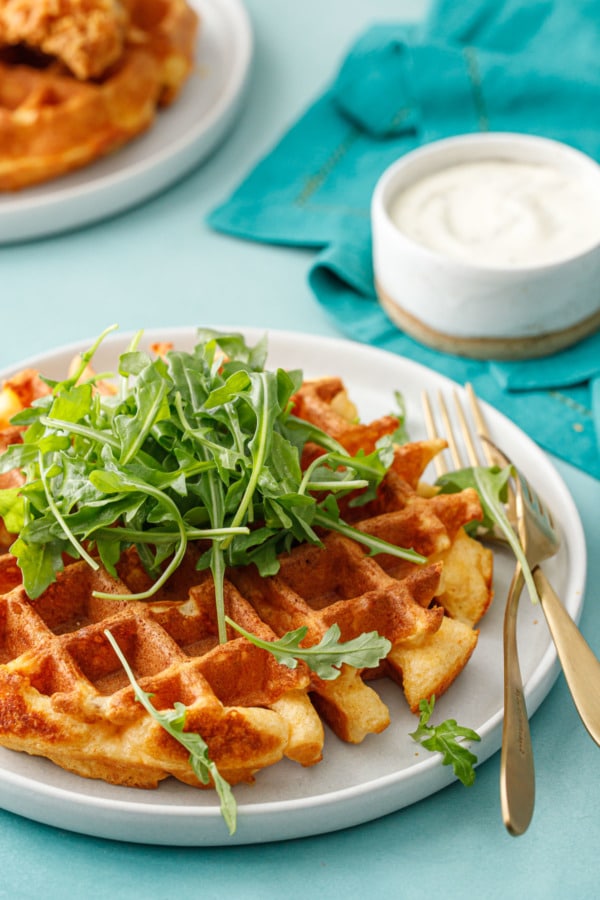Plate with a full round Savory Cheddar Cheese Waffles, topped with a pile of baby arugula