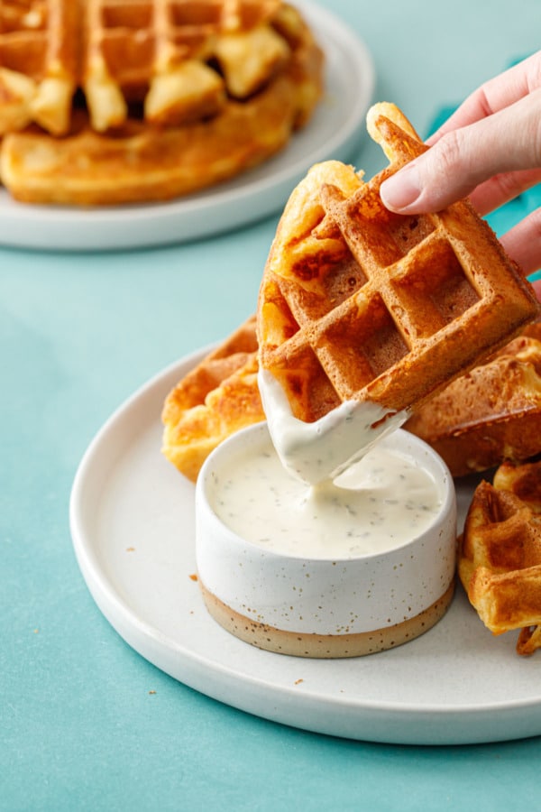 Dipping one piece of a Savory Cheddar Cheese Waffle into a cup of ranch dressing