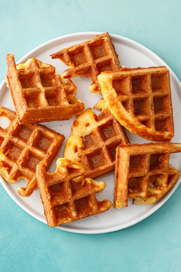 Overhead, white plate with pieces of Savory Cheddar Cheese Waffles, on a turquoise background