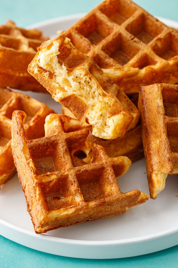 Plate of quarter round pieces of Savory Cheddar Cheese Waffles, one split in half to show the fluffy interior texture