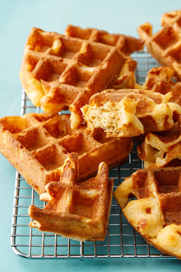 Stack of thick belgian cheese wafles, one with a bite to show the light and fluffy texture.