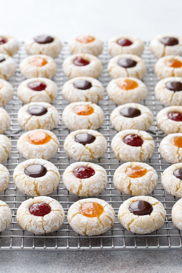 Rows of Amaretti Thumbprint Cookies in neat rows on a wire rack, alternating between three kinds of filling.